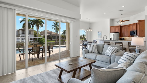 A spacious living area with a large sliding glass door leading to a poolside patio, a kitchen with wooden cabinets, and a ceiling fan.