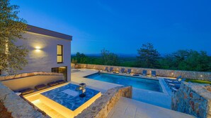 A modern outdoor pool area with a stone wall, lounge chairs, and a view of the landscape. - Amazing home in Vrh with sauna (Vrh)