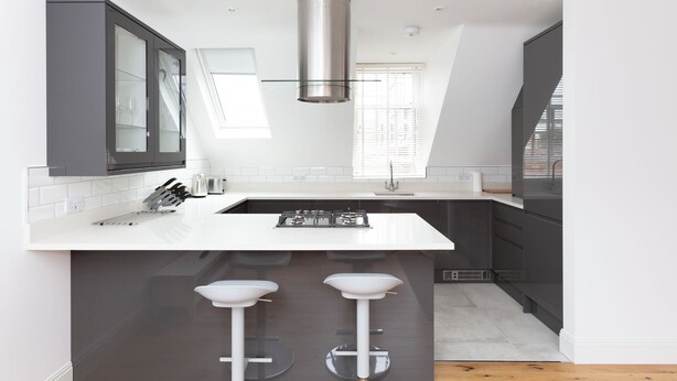 A modern kitchen with a central island, two bar stools, a stainless steel range hood, and a window with blinds. - Hampden Apartments - The William (Windsor)