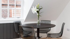 A dining area with a round table, four chairs, and a vase with flowers. - Hampden Apartments - The William (Windsor)