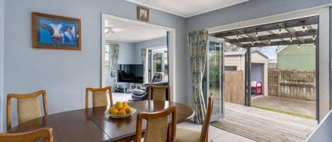A dining area with a round table, chairs, and a bowl of fruit. There is a large window and a door leading to a patio.
