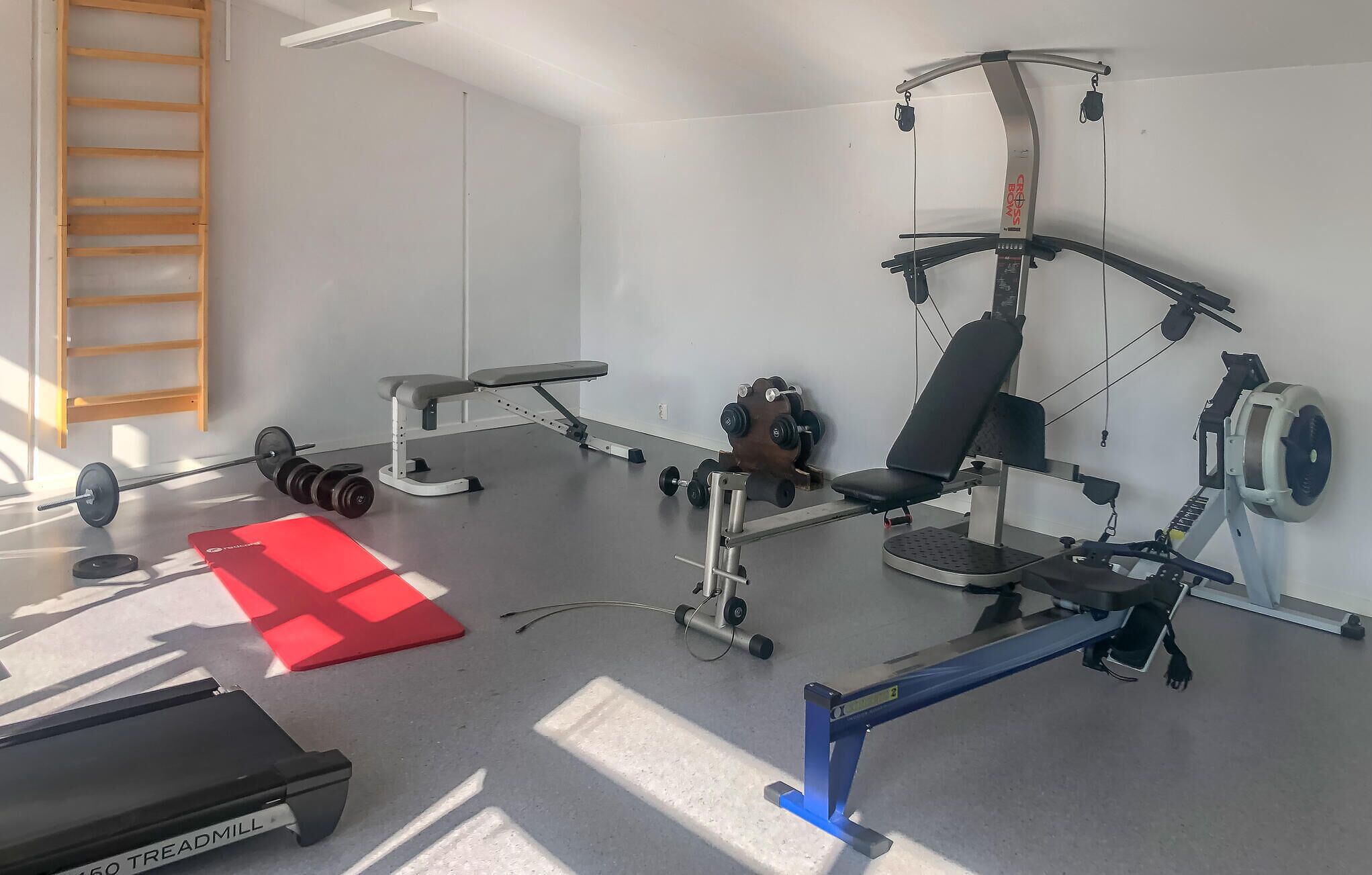 Un gimnasio con cinta de correr, banco de pesas y diverso equipamiento de ejercicio.