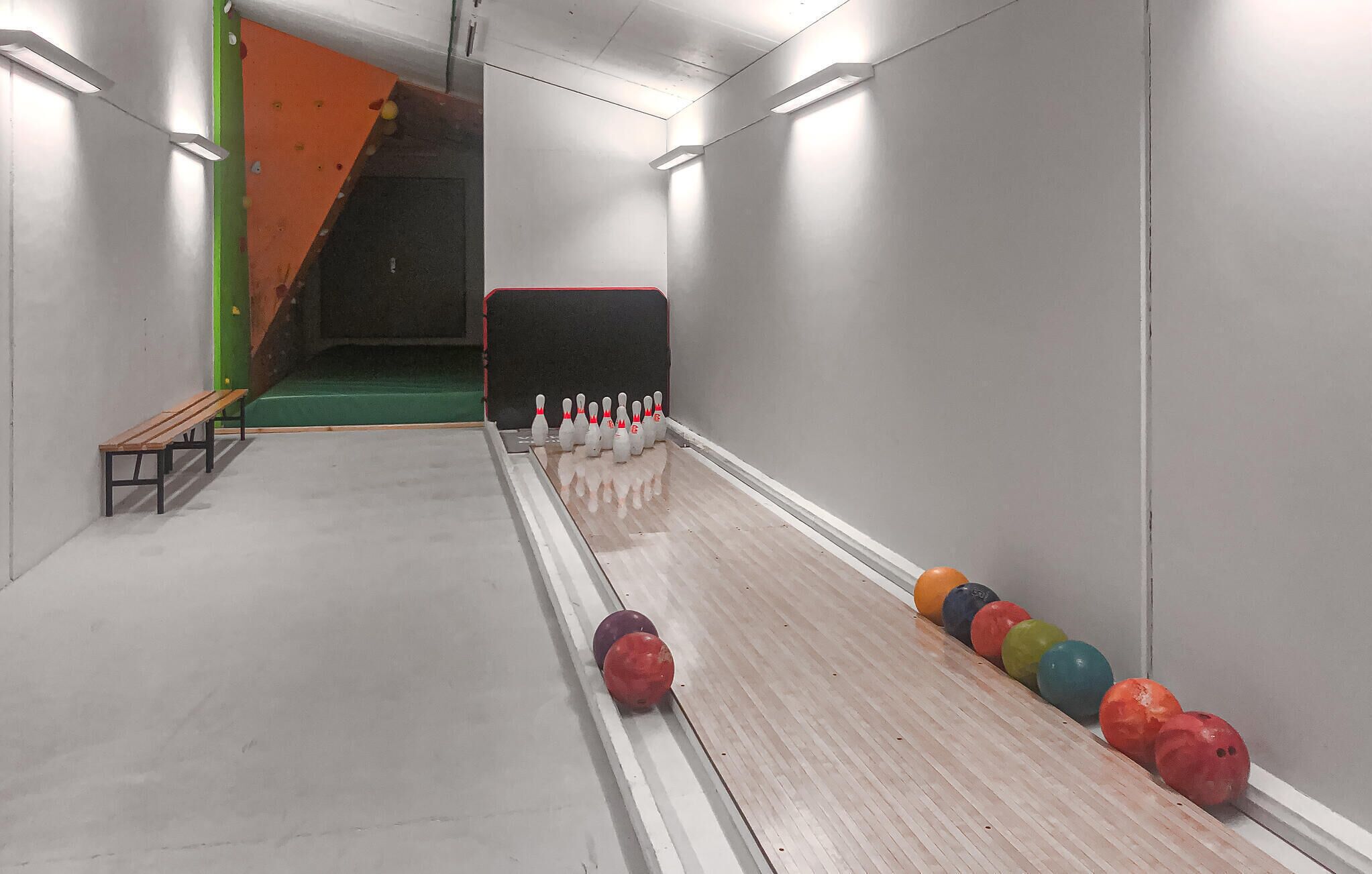 Une salle de bowling avec un plancher en bois, une zone recouverte d’une moquette verte et une rangée de quilles colorées.