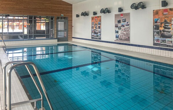 Una piscina interior con agua azul cristalina, una escalera de metal y paredes con azulejos.