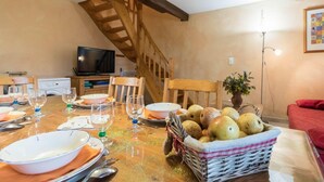 Ein Essbereich mit einem Holztisch, der für eine Mahlzeit gedeckt ist, einem Fernseher im Hintergrund und einer Treppe.