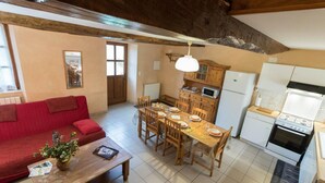 Ein gemütliches Wohnzimmer mit rotem Sofa, Esstisch aus Holz und einer Küchenzeile mit Holzschränken und Geräten.