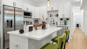 Una cocina moderna con gabinetes blancos, electrodomésticos de acero inoxidable y una isla central con taburetes de bar.