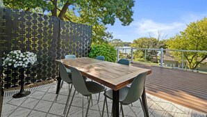 Un patio al aire libre con una mesa y sillas de madera, rodeado por un muro decorativo y follaje.