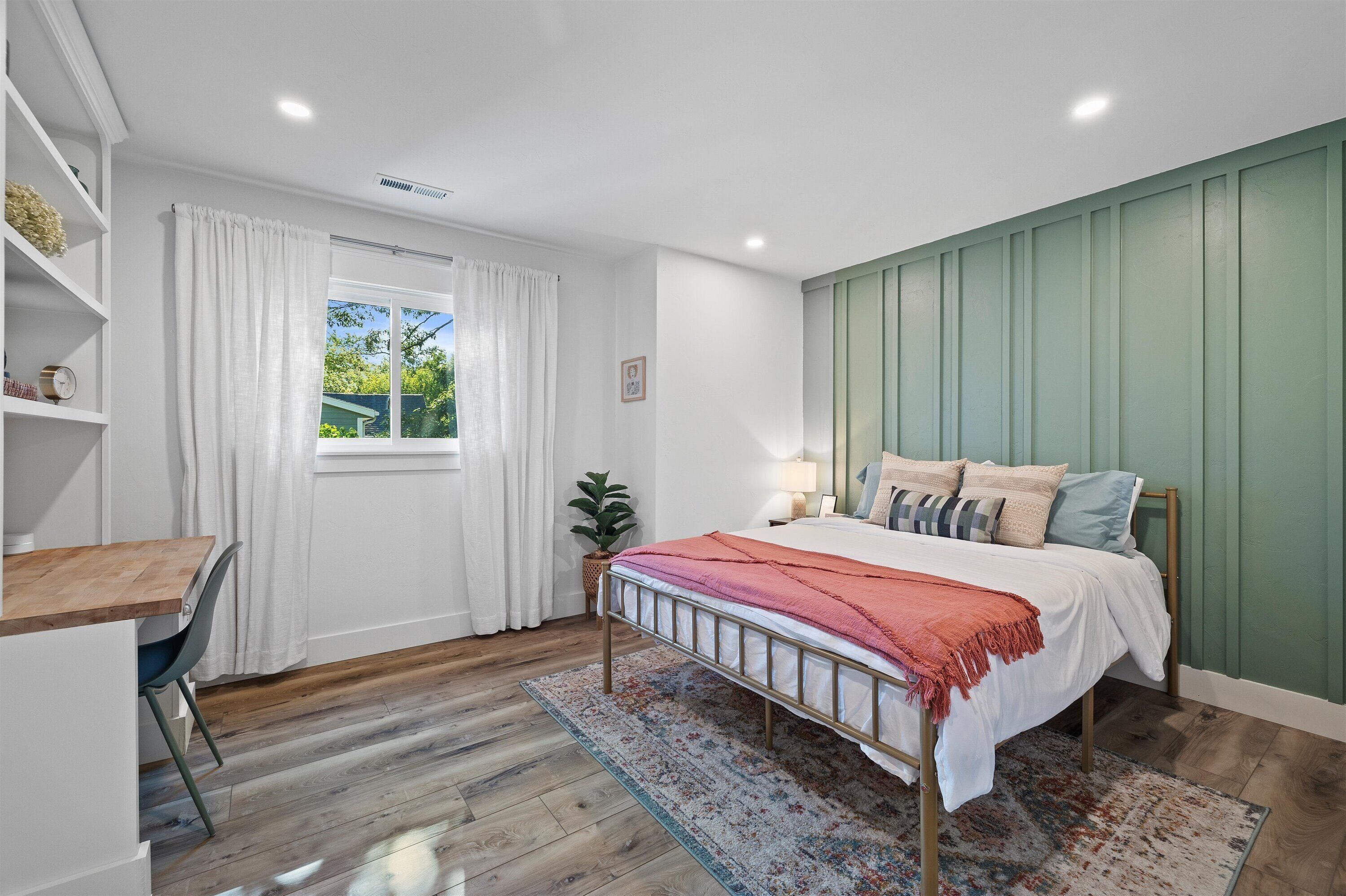 A bedroom with a bed, a desk, and a window with curtains.