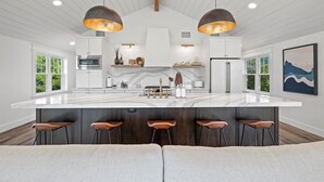 Una cocina moderna con una isla grande, taburetes de bar e iluminación colgante.