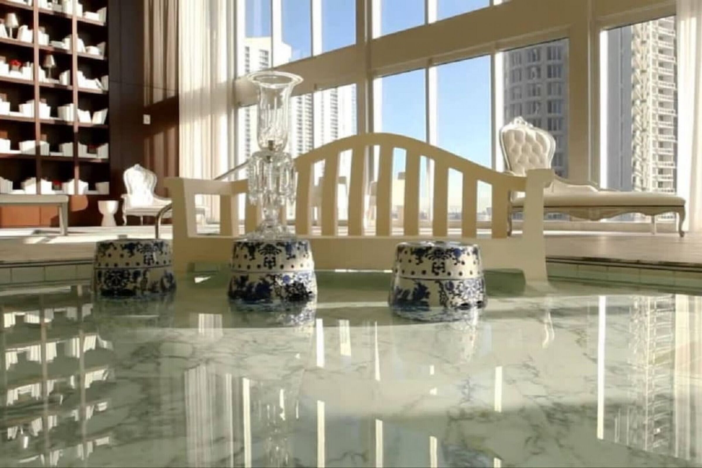 Un moderno vestíbulo de hotel con una mesa de mármol, jarrones decorativos, una araña y una estantería.