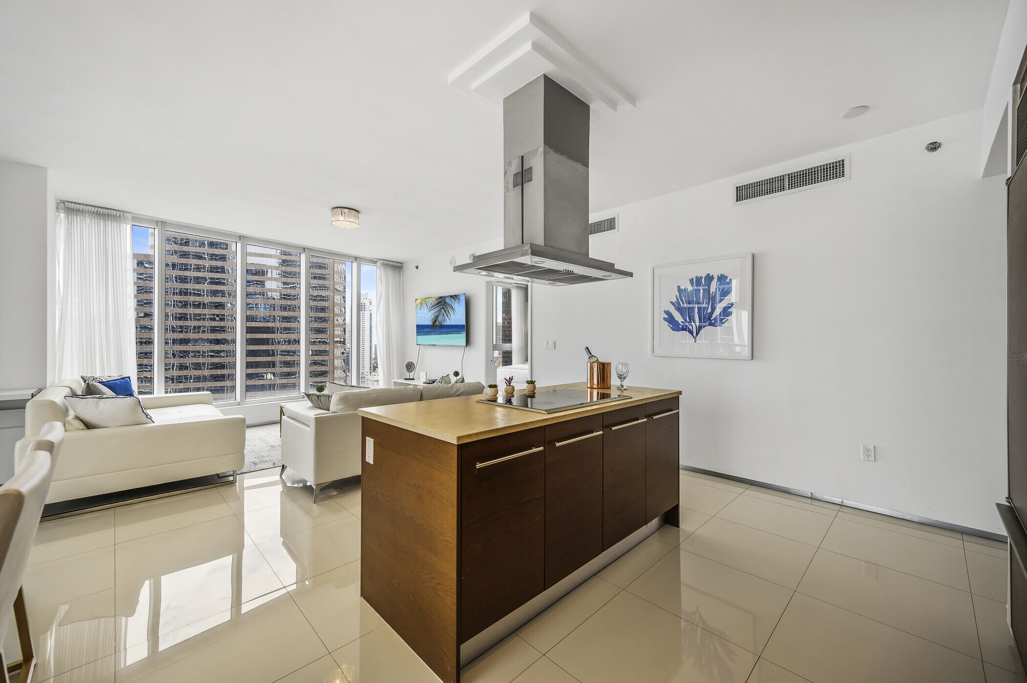 Cozinha moderna com ilha central, paredes brancas e grandes janelas.