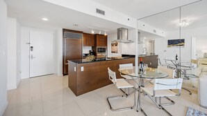 A modern kitchen with a central island, stainless steel appliances, and a dining area with glass tables and chairs.