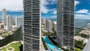Un immeuble de grande hauteur doté d’une façade en verre, d’une piscine et offrant une vue sur le paysage urbain et les étendues d’eau environnantes.