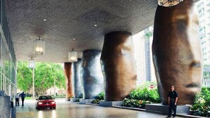 Un bâtiment moderne, orné de grandes sculptures abstraites, avec une voiture rouge garée devant.