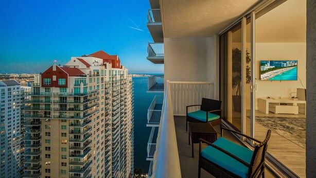 A balcony with a view of the sea, a television, and a seating area with cushions. - The Club 3904 · High Floor Unit Located in Brickell - Free Parking (Miami)