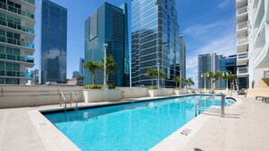 A swimming pool with a clear blue water surface, surrounded by modern high-rise buildings and palm trees. - The Club 3904 · High Floor Unit Located in Brickell - Free Parking (Miami)