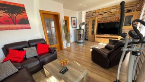 Ein Wohnzimmer mit Sofa, Couchtisch, Fernseher, Kamin und Trainingsgeräten.