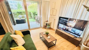 A living room with a green sofa, a coffee table, and a flat-screen TV displaying a program. - Chic one bedroom with parking&terrace (Luxembourg City)