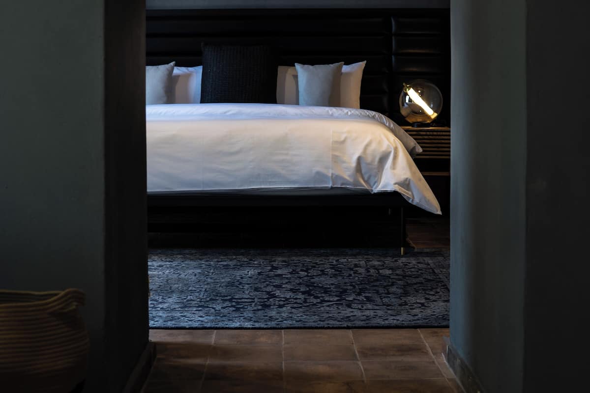 Un dormitorio con cama, almohadas, mesita de noche y lámpara.