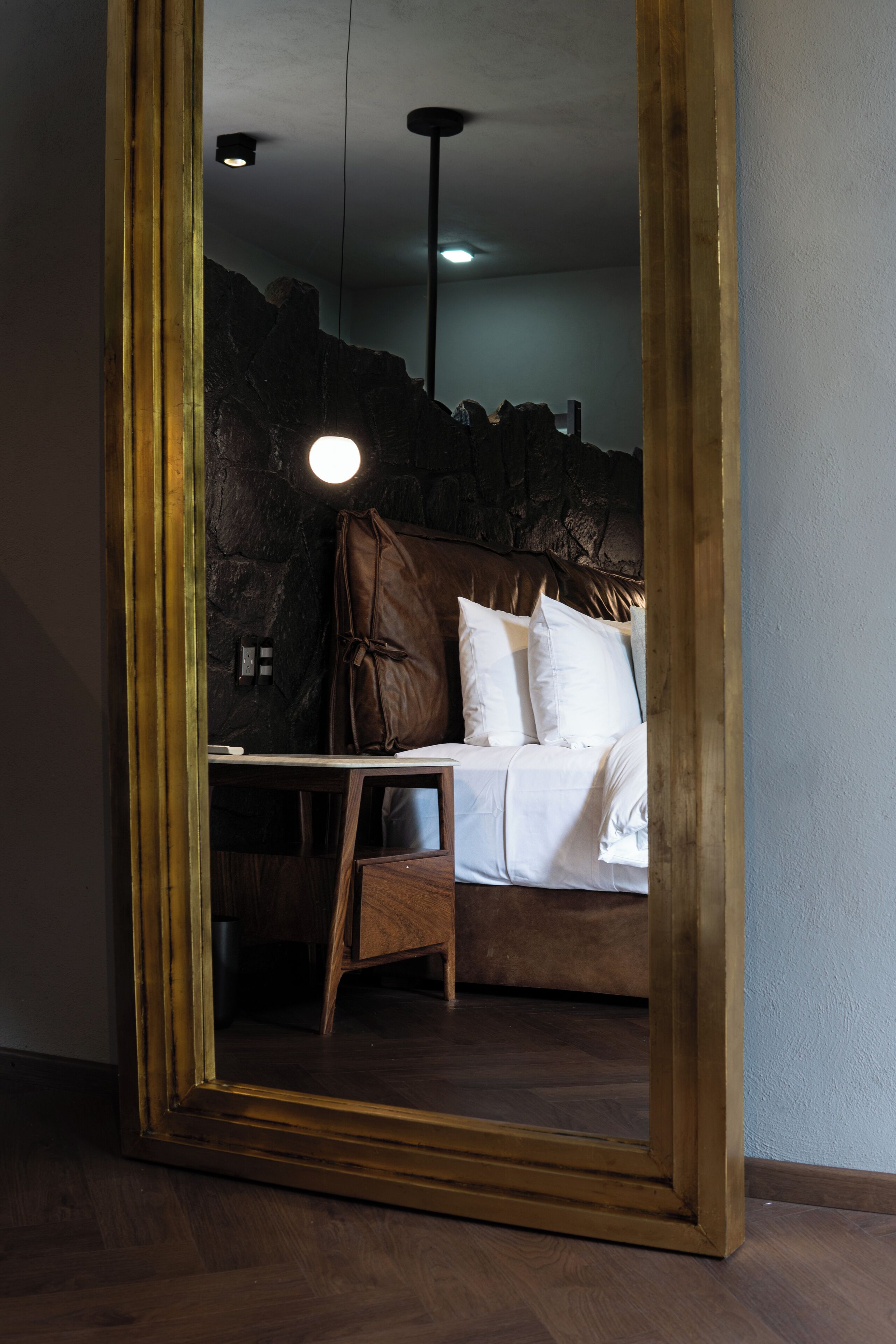 A bedroom with a bed, a nightstand, and a mirror reflecting the room.