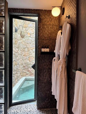 Une salle de bain avec un mur en pierre, une porte en verre donnant sur l’extérieur et un porte-serviettes avec des serviettes blanches.