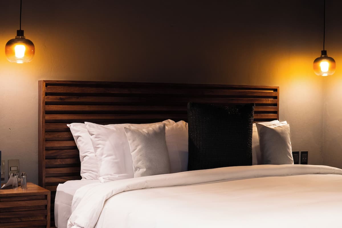 Un dormitorio moderno con cabecera de madera, ropa de cama blanca y dos lámparas colgantes.