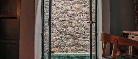 Una habitación con pared de piedra, una silla de madera y suelo de baldosas.