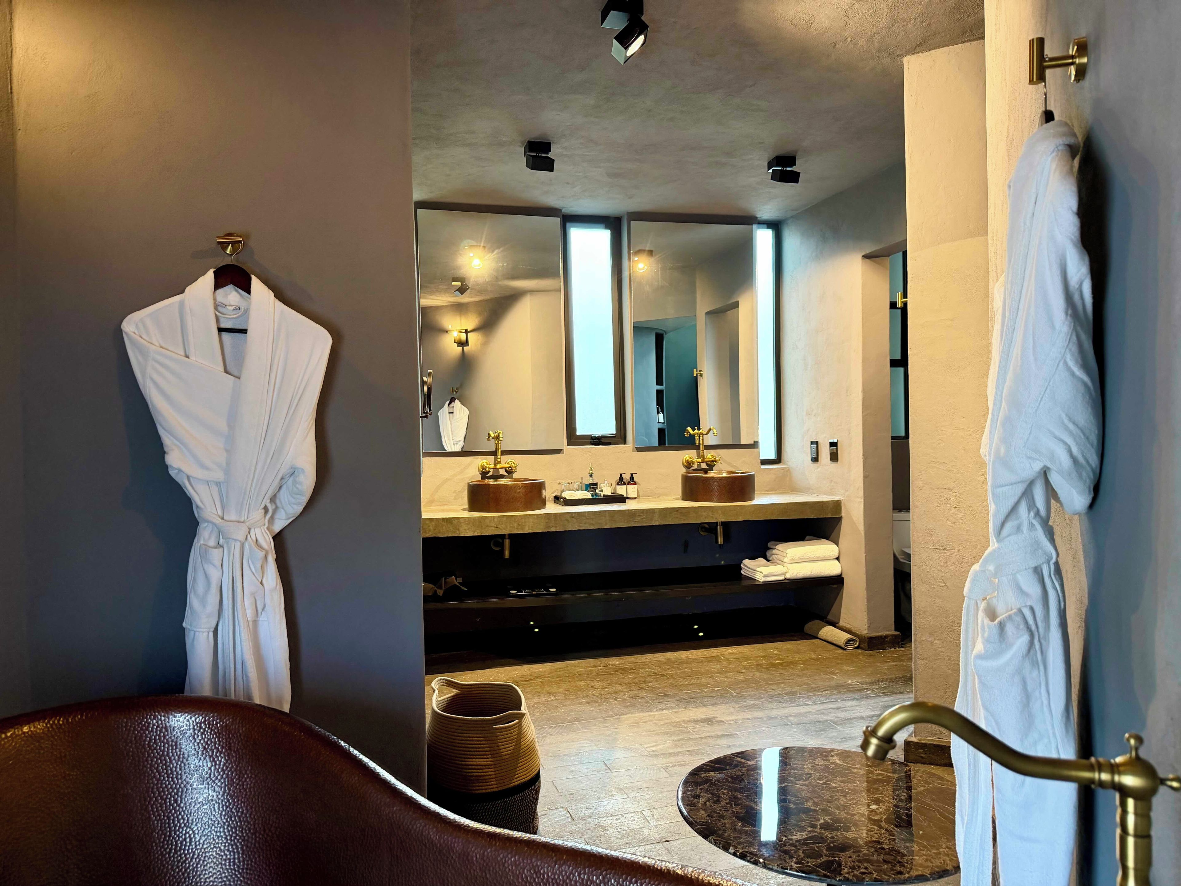 A modern bathroom with a bathtub, a vanity with a large mirror, and two white robes hanging on hooks.