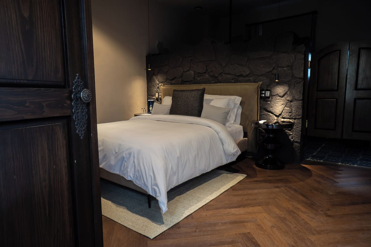 Un dormitorio con una cama grande, una pared de piedra y piso de madera.