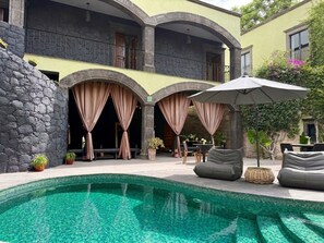 Un área de piscina con un muro de piedra, una silla de salón y una mesa con sombrillas.