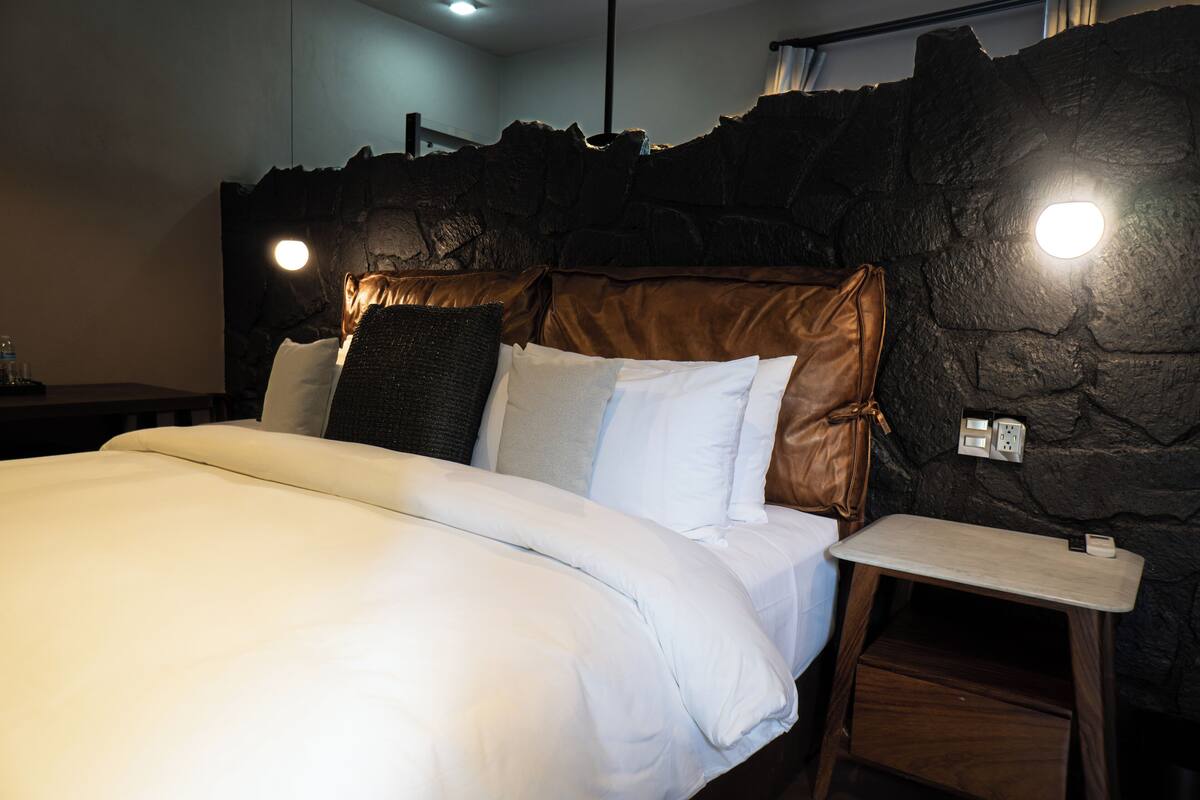 Una cama bien hecha con ropa blanca, un cabecero marrón y una mesita de noche con una lámpara.