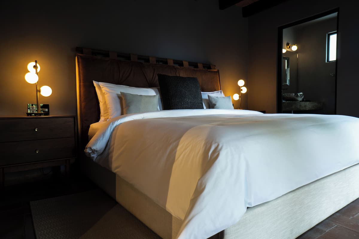 Una cama bien hecha con sábanas blancas, cabecera de madera y lámparas de noche.