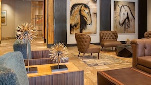 Un vestíbulo espacioso con un sofá de cuero marrón, dos sillones capitonados, una mesa de centro y una escultura decorativa.