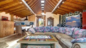 A cozy interior with a wooden ceiling, a large cushioned sofa, a dining table, and a kitchen area. - CASA VERDE Apartment 4 Detached small house. Sea view Risco Famara (CN)