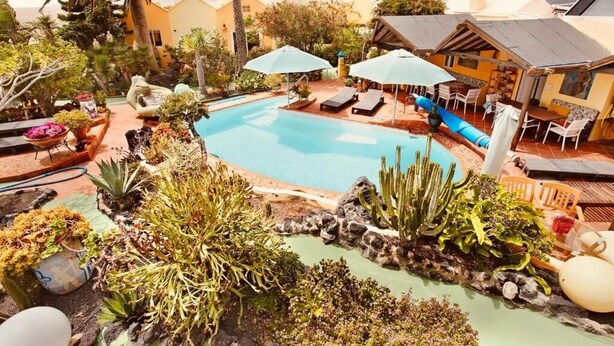 A pool area with lounge chairs and umbrellas, surrounded by various plants and a small waterfall feature. - CASA VERDE Apartment 4 Detached small house. Sea view Risco Famara (CN)