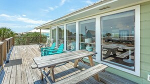Un terrazzo in legno con tavoli e sedie da picnic, ampie finestre e vista sull'oceano.
