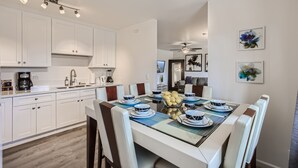 A modern kitchen with white cabinets, a dining table set with blue and white plates, and a ceiling fan. - NEW - Awesome 6BR - 15 Min To Beach (Oceanside)
