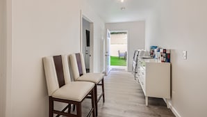 A hallway with two chairs, a white cabinet with items, and a door leading to a green outdoor area. - NEW - Awesome 6BR - 15 Min To Beach (Oceanside)