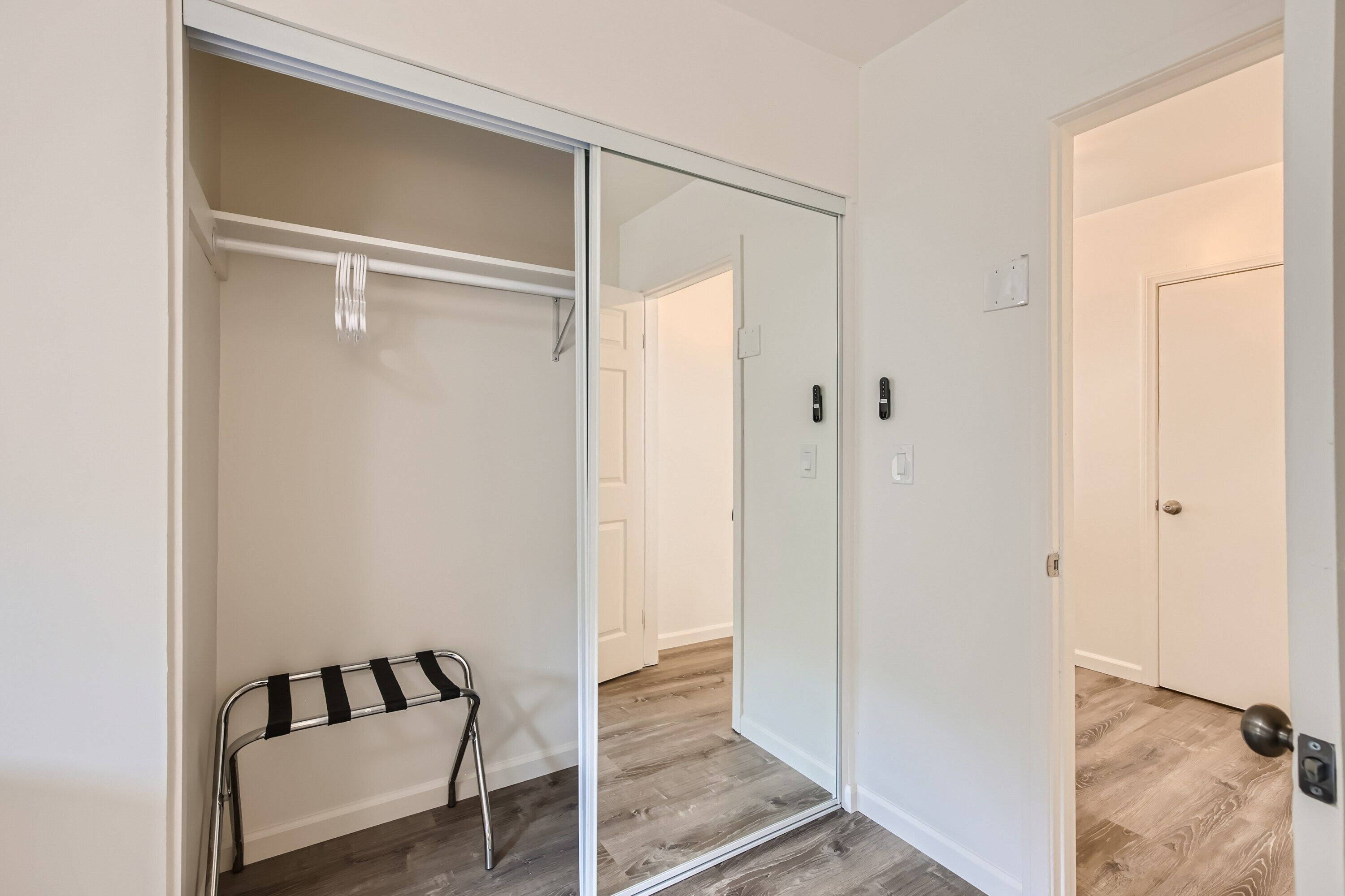 Un pasillo con una puerta corredera para armario, un banco y un espejo que refleja la puerta.