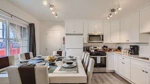 A modern kitchen with white cabinets, a microwave, stove, and a dining area with a table set for four. - NEW - Awesome 6BR - 15 Min To Beach (Oceanside)