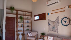 Uma sala de estar com estante de madeira, sofá com almofadas decorativas e decoração náutica nas paredes.