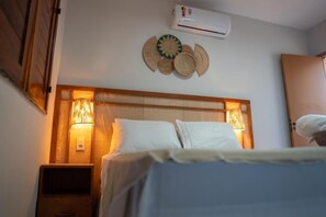 Ein Hotelzimmer mit Bett, zwei Nachttischlampen, einer Wand-Klimaanlage und einem Wandbild.