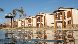 Um resort com vários edifícios de dois andares, uma piscina e palmeiras.