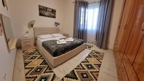 A bedroom with a bed, bedside tables, a mirror, a painting, and a window with curtains.