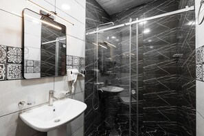 A modern bathroom with a glass-enclosed shower, a white sink, and patterned tiles.