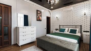 Un dormitorio moderno con pared de ladrillo, un tocador blanco, cama con ropa de cama verde y un candelabro.