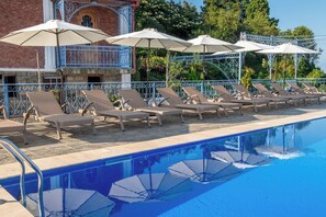 A poolside area with lounge chairs and umbrellas, a brick building with a balcony, and a clear blue pool.