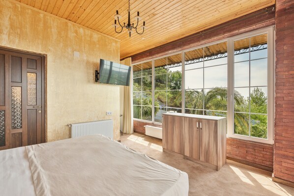 Een slaapkamer met een groot bed, een aan de muur bevestigde televisie en een balkon met uitzicht op groen.