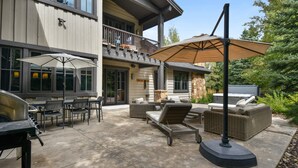 Une terrasse extérieure équipée d’un barbecue, de chaises de salle à manger, d’un canapé et d’un grand parasol.